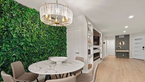 Ein modernes Interieur mit einem runden Marmortisch, beigen Stühlen, einer grünen Wand mit Pflanzen und einer Pendelleuchte.