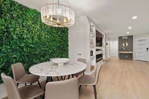 En modern inredning med ett runt bord i marmor, beige stolar, en grön vägg med växter och en kristallkrona.