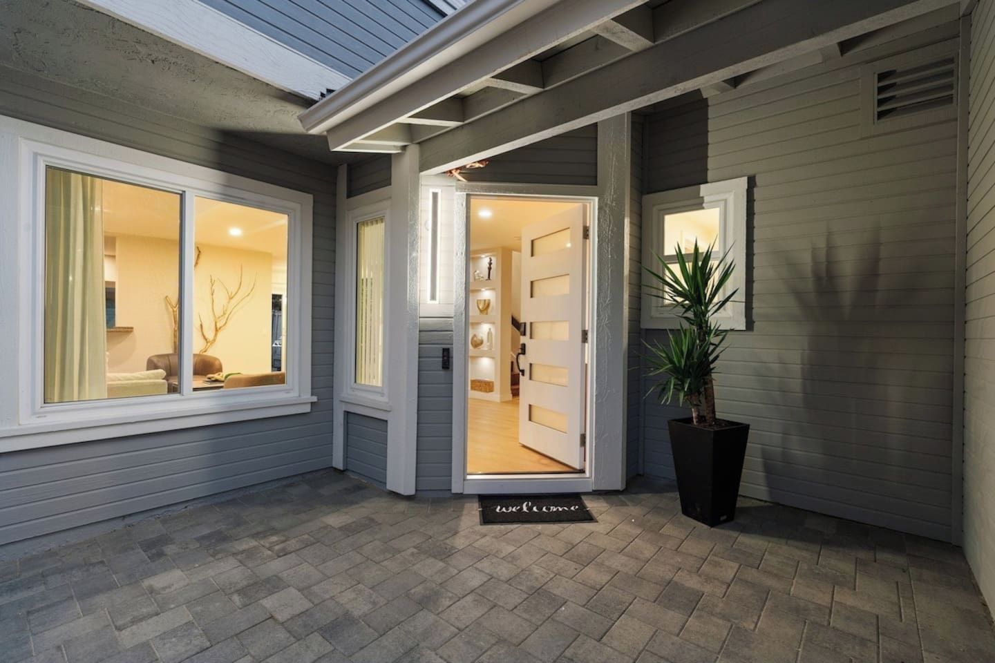 Une entrée de maison avec un paillasson, une plante en pot et une vue sur l’intérieur.