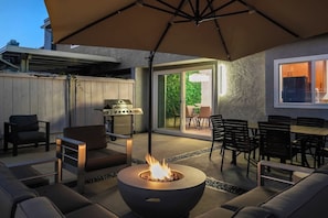 An outdoor patio with a fire pit, seating, and a grill.
