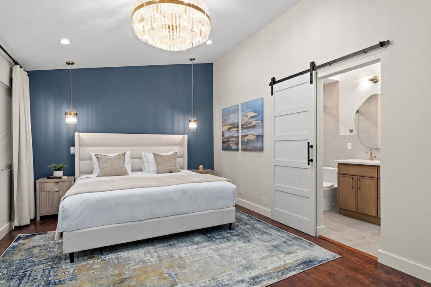 Une chambre à coucher avec un grand lit, un lustre, une porte coulissante donnant accès à la salle de bain et des œuvres d’art accrochées au mur.