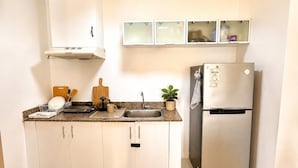 Eine Küche mit weißen Schränken, einer Spüle aus Edelstahl, einem Kühlschrank und einer Arbeitsplatte mit Geschirrständer und Besteck.