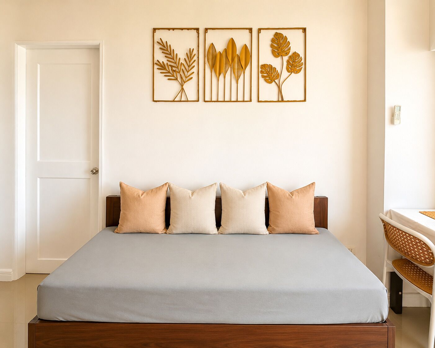 A bed with a light blue bedspread, a wooden headboard, and four pillows. There are three framed botanical prints on the wall above the bed.