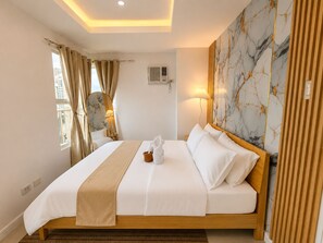 Camera d'albergo con un letto, tende, uno specchio, una lampada e una parete con motivo marmorizzato.