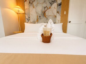 Una camera d'albergo con un letto, un comodino, una lampada, una parete con decoro marmorizzato e un cesto con un asciugamano e un opuscolo.