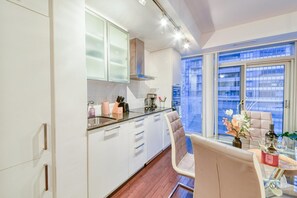 Una cocina moderna con armarios blancos, un lavamanos de acero inoxidable y una zona de comedor con mesa y sillas de vidrio.