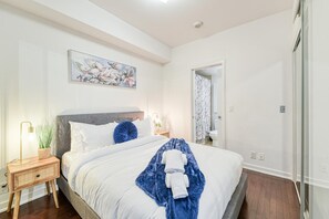A bedroom with a bed, bedside table, lamp, and a painting on the wall. - Comfort 1BR Hotel Suite at The Velaire Toronto | Sleeps 4 (Toronto)