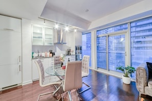 A modern kitchen with a glass dining table, chairs, and a view of the city through large windows. - Comfort 1BR Hotel Suite at The Velaire Toronto | Sleeps 4 (Toronto)