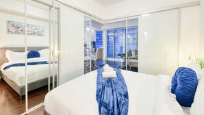 Ein modernes Hotelzimmer mit einem großen Bett, einem Schreibtisch und Blick auf die Stadt durch eine Glaswand.