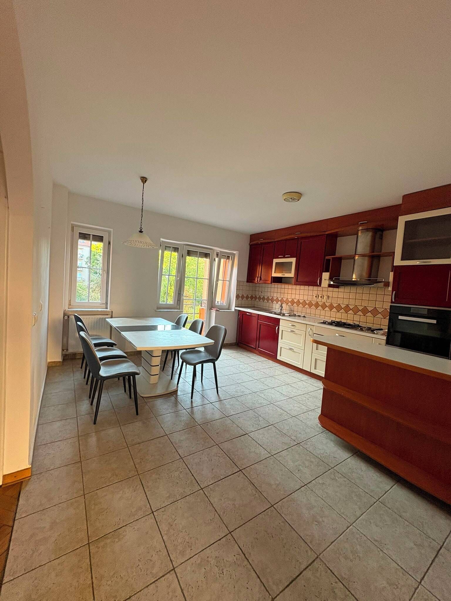 A spacious kitchen with a dining area, large windows, and a tiled floor.