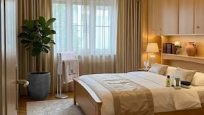 Un dormitorio de hotel con cama, una planta en maceta, una mesita de noche y un ventanal con cortinas.
