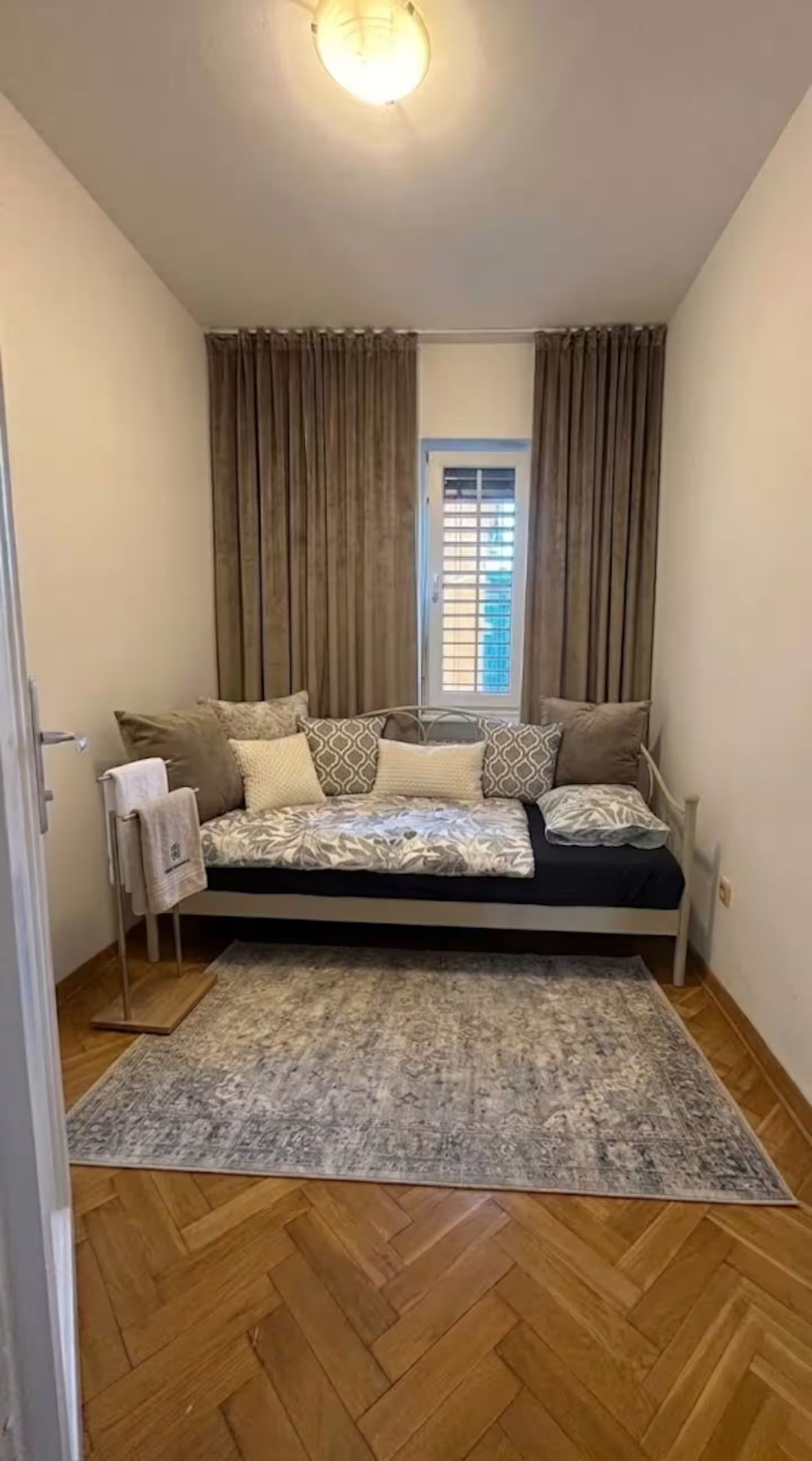 A small bedroom with a bed, curtains, a window, and a patterned rug.