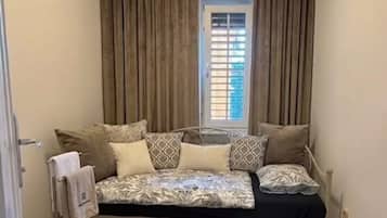 A small bedroom with a bed, curtains, a window, and a patterned rug.