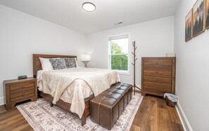Quarto com cama, mesas de cabeceira, um banco, cômoda e janela.