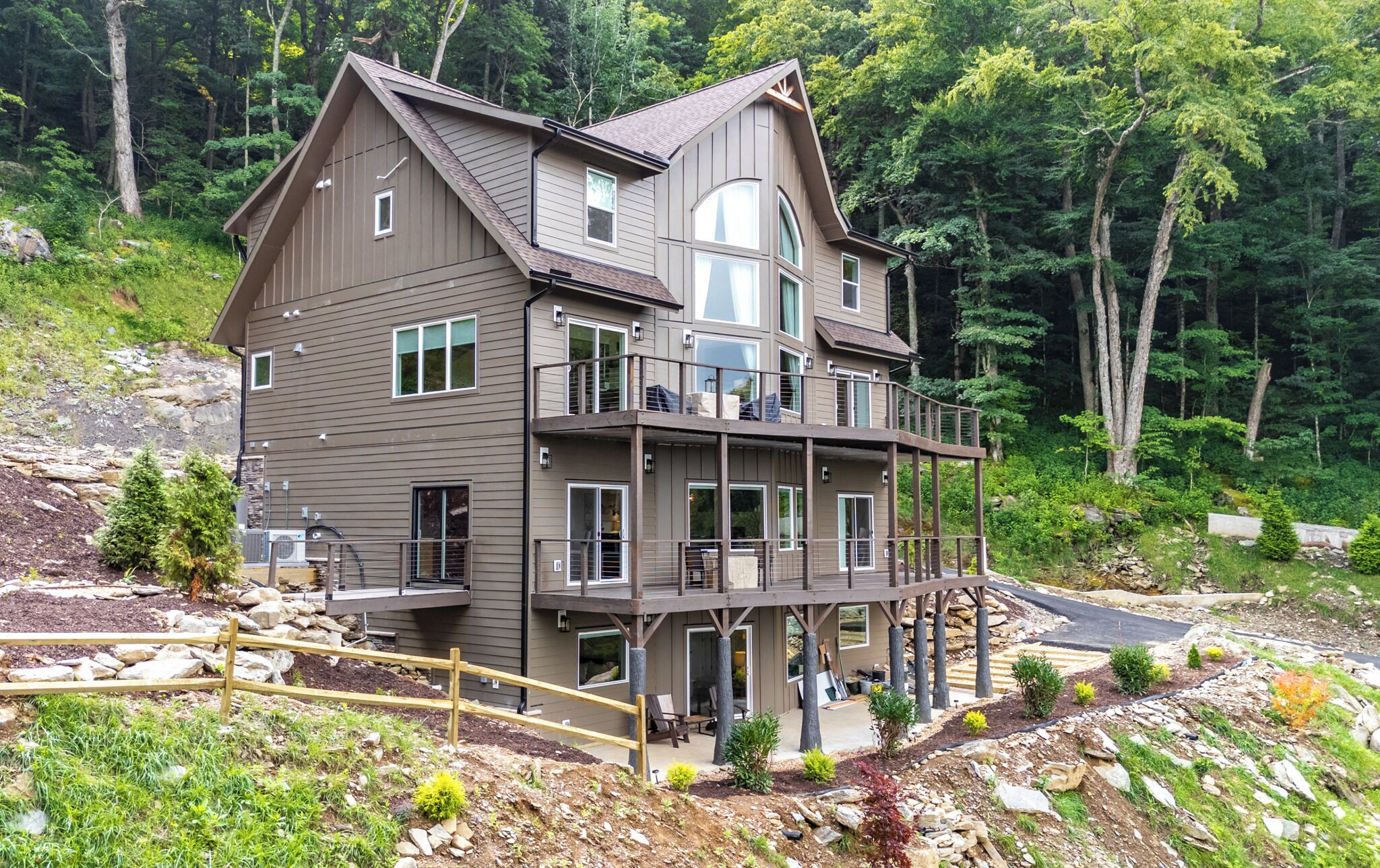A multi-story house with a balcony, surrounded by a forested landscape.
