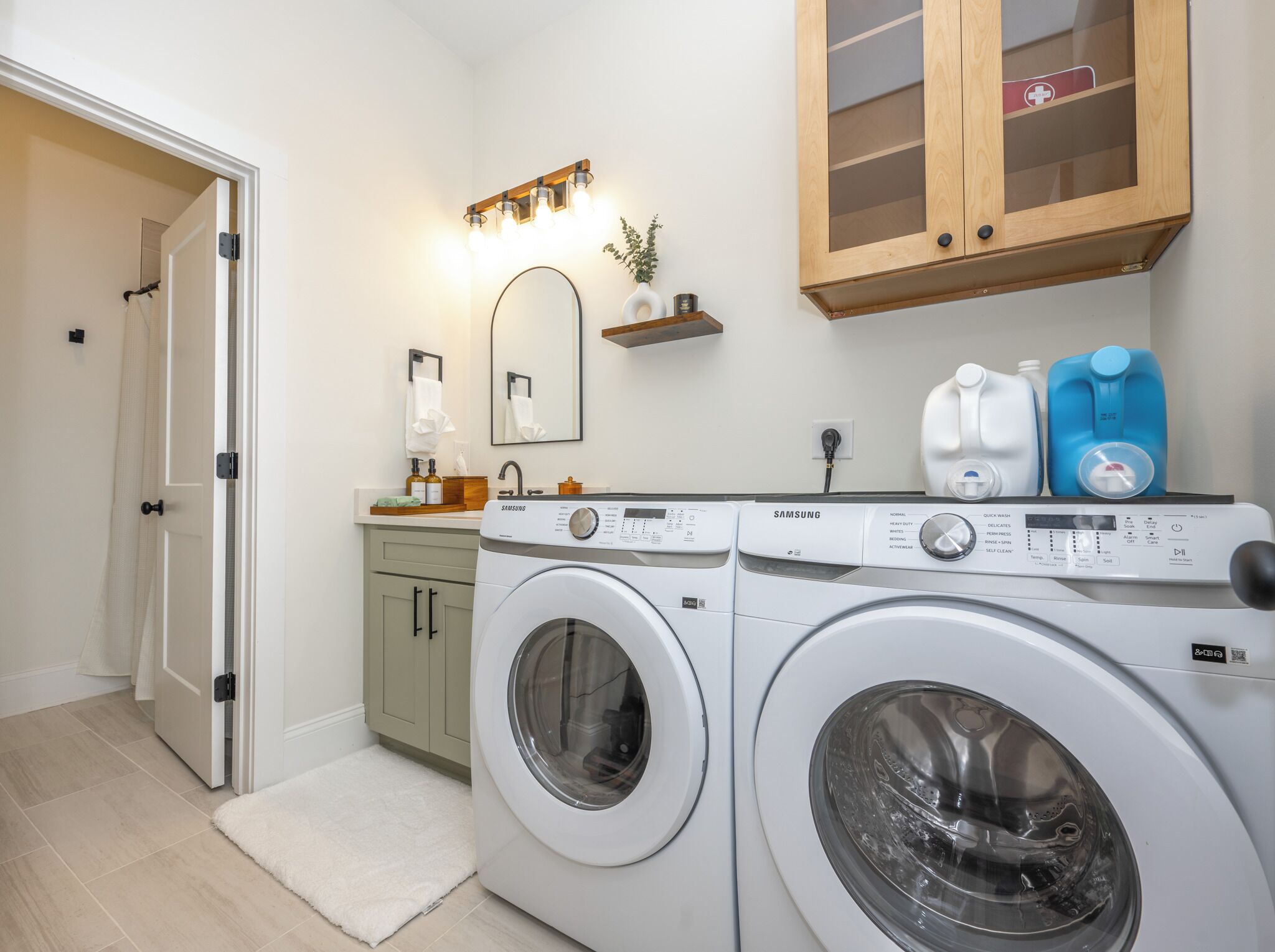 A laundry room with two front-loading washing machines, a sink, a mirror, and a shelf with toiletries.