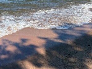 A sandy beach with gentle waves and tree shadows. - Loon Cabin – Gichigami Island Properties (La Pointe)