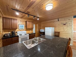 A wooden cabin interior with a kitchen area featuring a stove, sink, and cabinets. - Loon Cabin – Gichigami Island Properties (La Pointe)