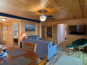 A cozy cabin interior with a wooden ceiling, a sofa, a dining table, and a television. - Loon Cabin – Gichigami Island Properties (La Pointe)