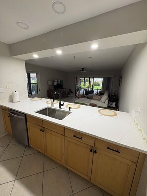 A modern kitchen with a central island, a dishwasher, and a large window offering a view of the outdoors. - Charming Coastal 1-bedroom condo in wonderful Nokomis, 1 mile from the beach! (Nokomis)