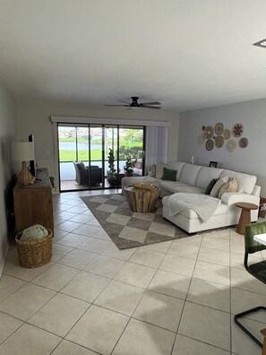 A spacious living room with a large sofa, a coffee table, and a view through a sliding glass door to the outdoors. - Charming Coastal 1-bedroom condo in wonderful Nokomis, 1 mile from the beach! (Nokomis)