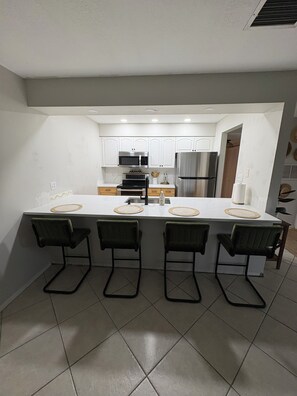 A modern kitchen with white cabinets, stainless steel appliances, and a central island with bar stools. - Charming Coastal 1-bedroom condo in wonderful Nokomis, 1 mile from the beach! (Nokomis)
