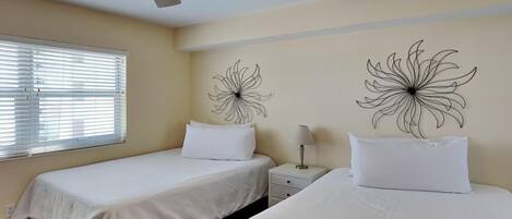 Une chambre d’hôtel avec deux lits, un ventilateur de plafond et des œuvres d’art murales.