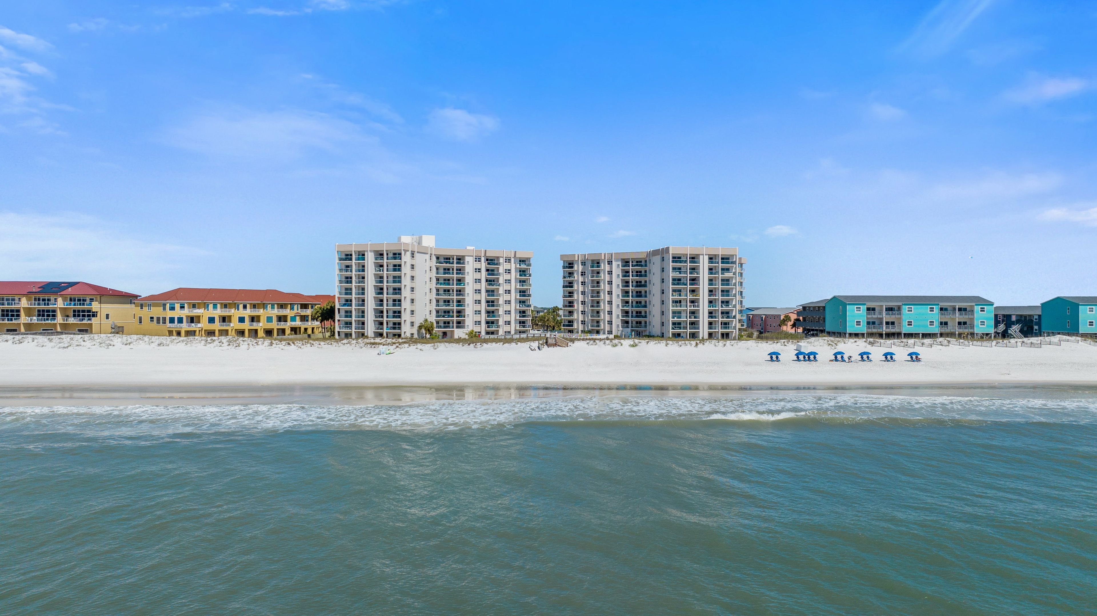 A beachfront hotel with multiple high-rise buildings, a sandy beach, and a clear blue sky.