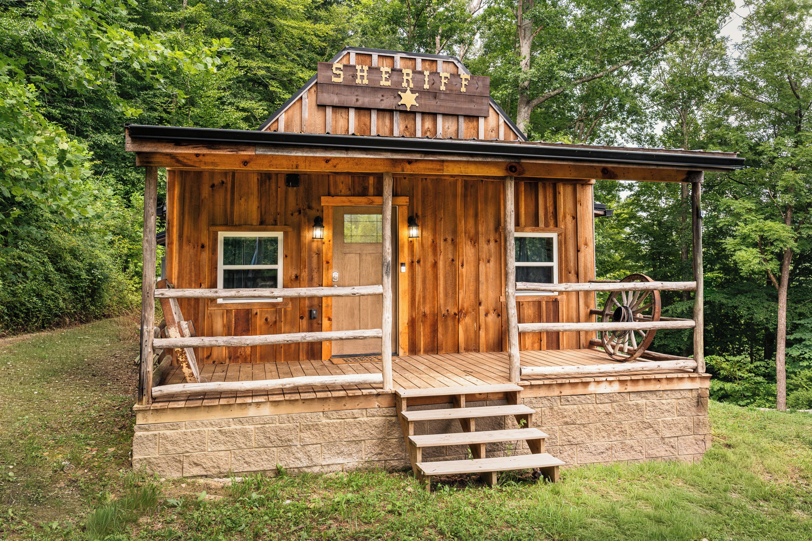 A wooden cabin with a porch, a front door, and a small window.