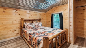 Ein Zimmer einer Holzhütte mit einem Bett, einem Fenster und einer Tür.