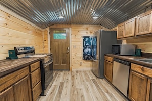 A compact kitchen with wooden cabinets, a refrigerator, a microwave, and a dishwasher. - Welcome to the Sheriff's Office (Stanton)