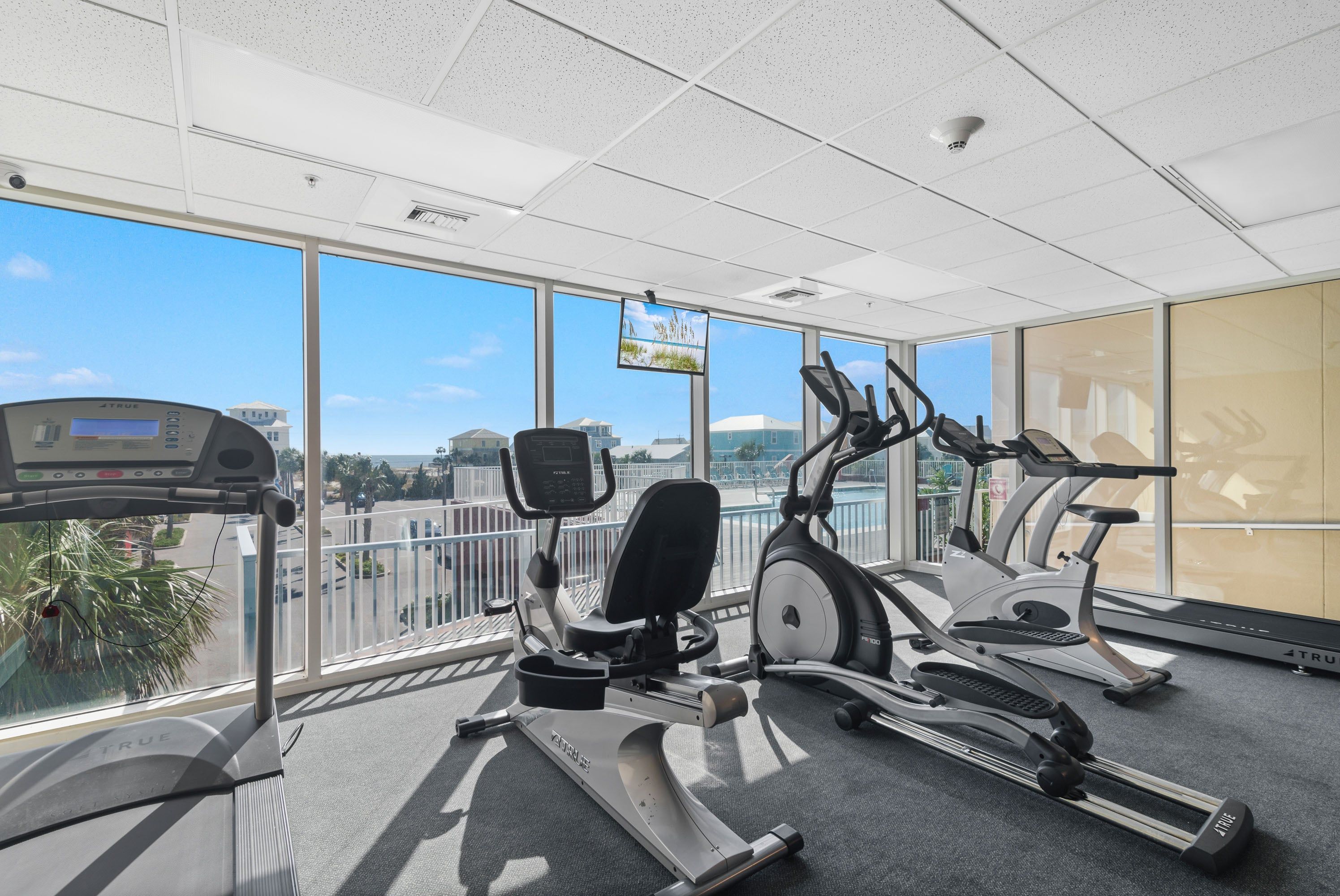 Un gimnasio con diversos equipos de ejercicio, grandes ventanales y vistas a la ciudad.