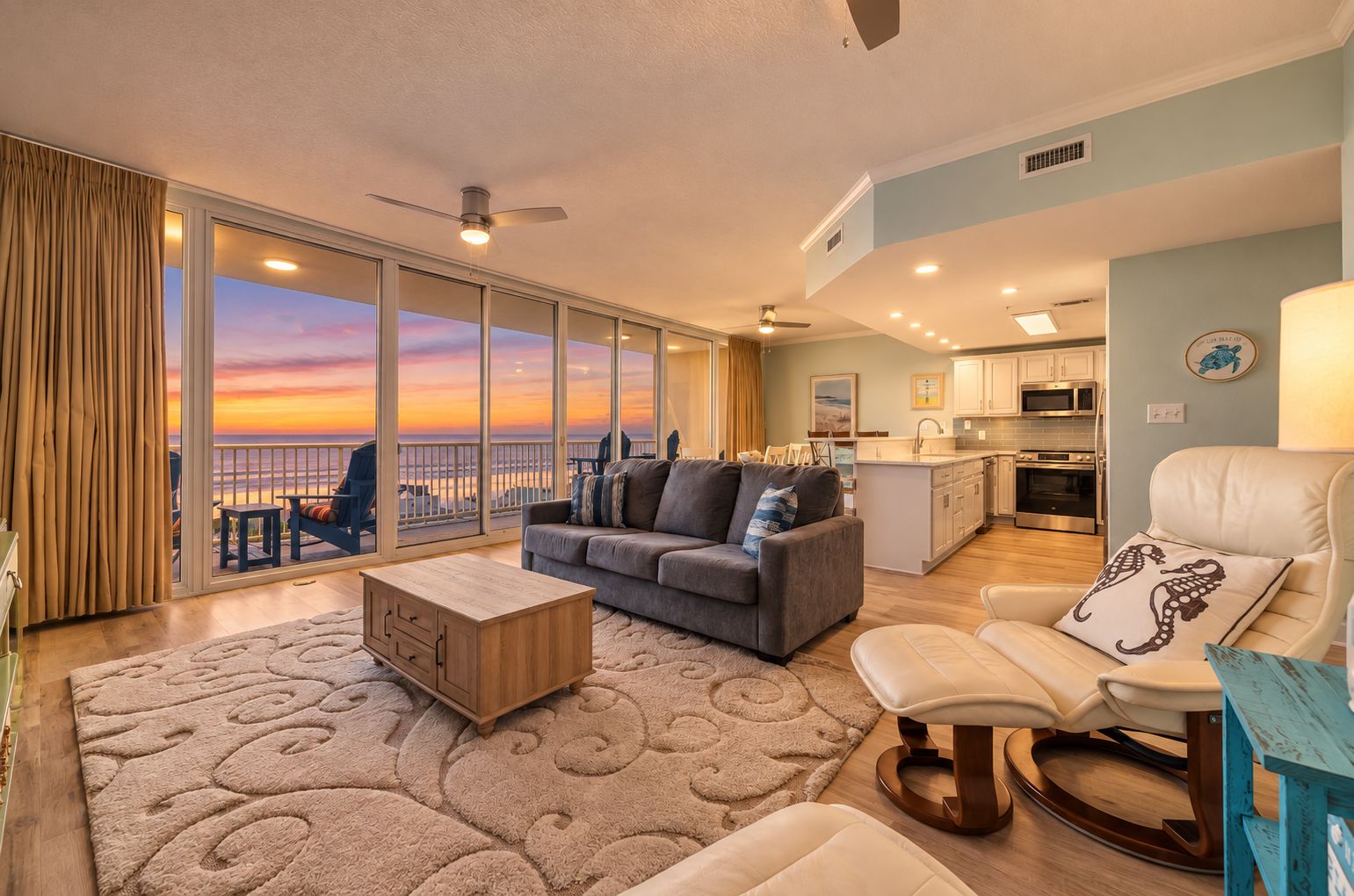 A spacious living area with a sofa, coffee table, and a view of the sunset through large windows.