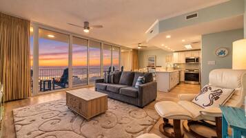 A spacious living area with a sofa, coffee table, and a view of the sunset through large windows.