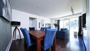 Ein moderner Essbereich mit einem Holztisch, blauen Stühlen, einer Couch und einem großen Fenster.