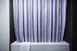 Un baño con cortina de ducha a rayas, una bañera blanca y paredes cubiertas de baldosas oscuras.