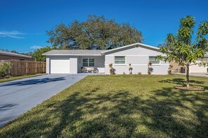 A single-story house with a garage, a front yard with grass and a small tree, and a wooden fence. - Peaceful 3-bedroom  2 full bath house with boat parking  15 min to the beach (Pinellas Park)