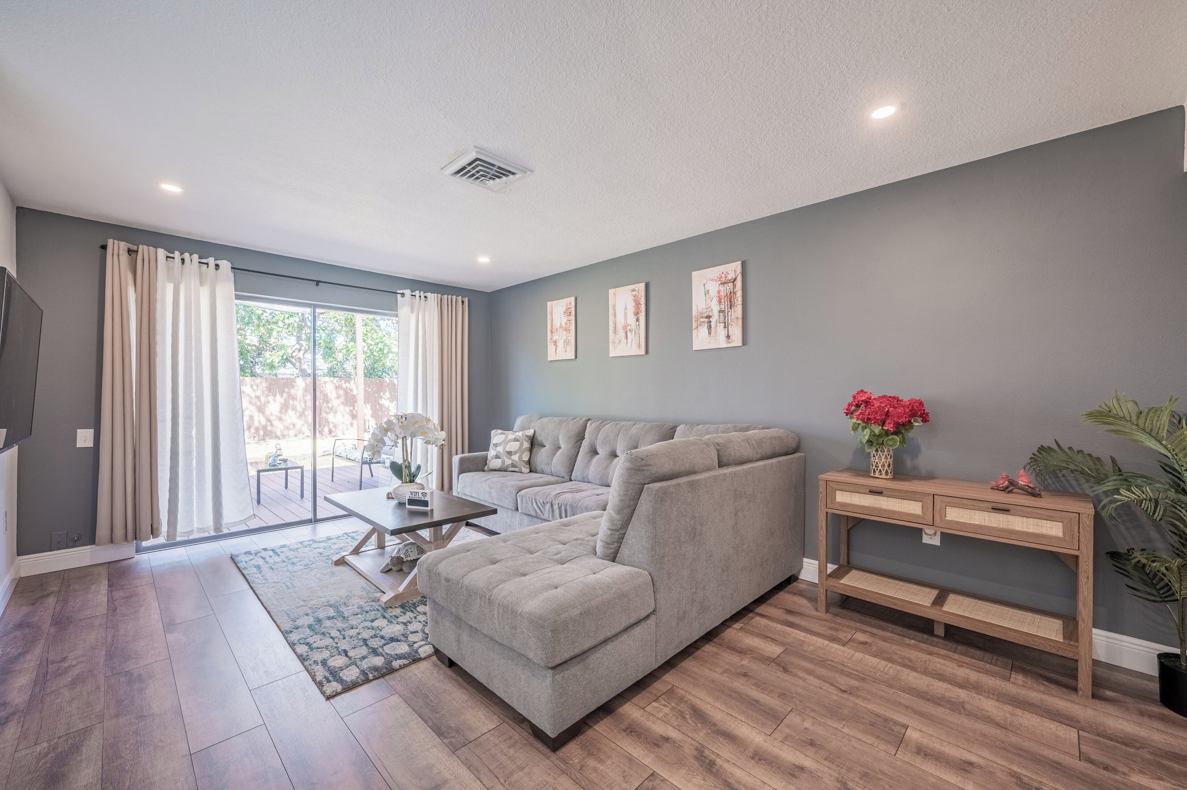 A modern living room with a grey sofa, a wooden coffee table, and a large window with curtains.