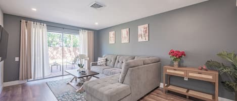 A modern living room with a grey sofa, a wooden coffee table, and a large window with curtains.