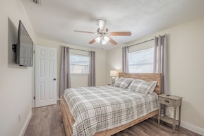 A bedroom with a bed, a nightstand, a ceiling fan, and a TV mounted on the wall. - Peaceful 3-bedroom  2 full bath house with boat parking  15 min to the beach (Pinellas Park)