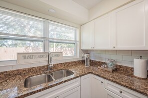 A kitchen with a granite countertop, stainless steel sink, white cabinets, and a window with blinds. - Peaceful 3-bedroom  2 full bath house with boat parking  15 min to the beach (Pinellas Park)