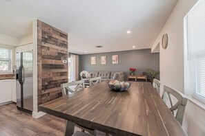A dining area with a wooden table, chairs, a bowl of fruit, a sofa, and a small side table with a vase of flowers. - Peaceful 3-bedroom  2 full bath house with boat parking  15 min to the beach (Pinellas Park)