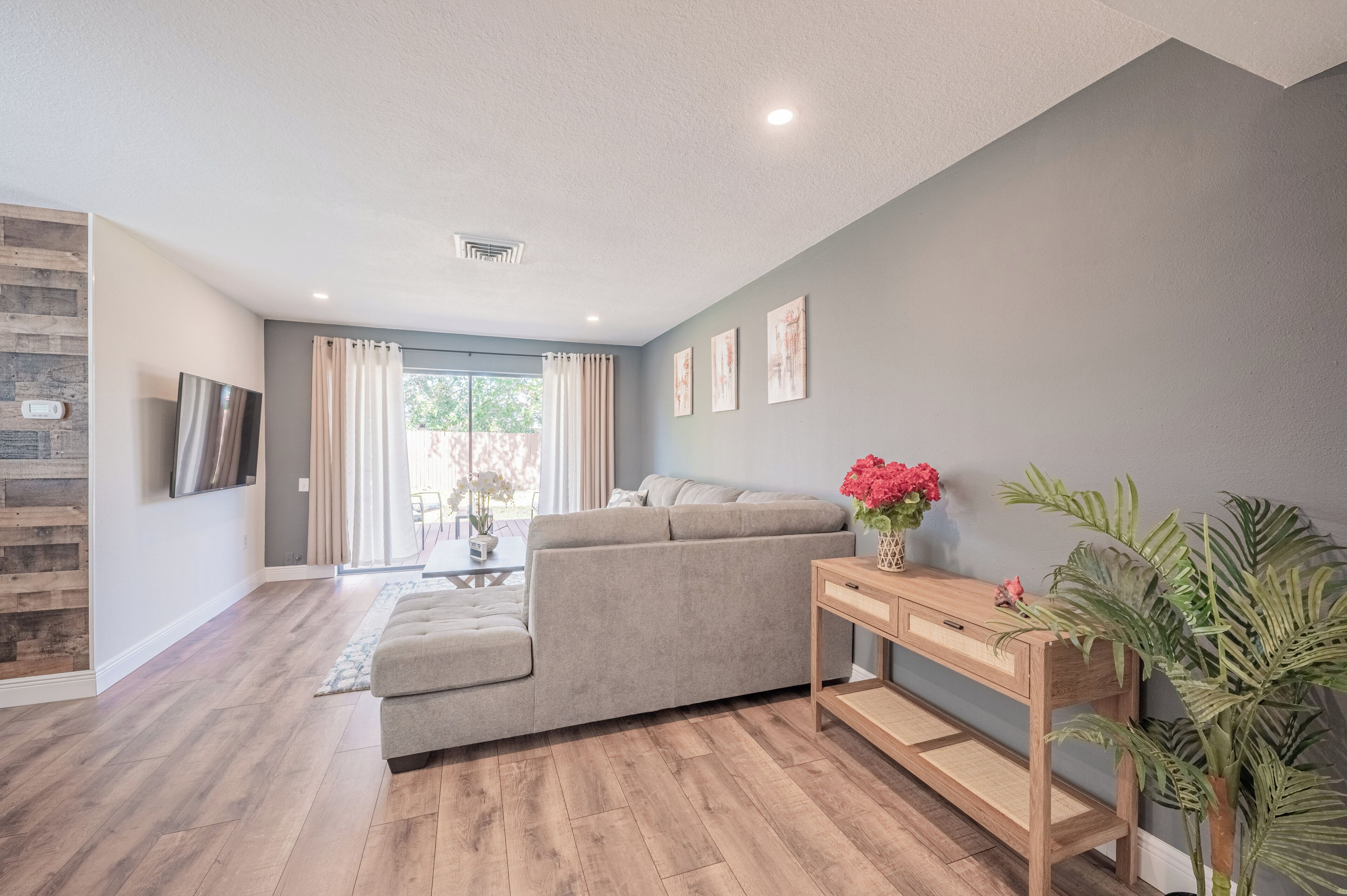 A modern living room with a grey sofa, a wooden coffee table, and a large window with curtains.