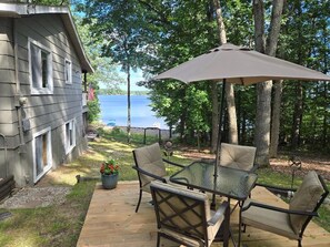 A deck with a glass table and chairs, an American flag, and a view of a lake. - Charming 3-bedroom house on Fife Lake perfect for enjoying any season (Fife Lake)