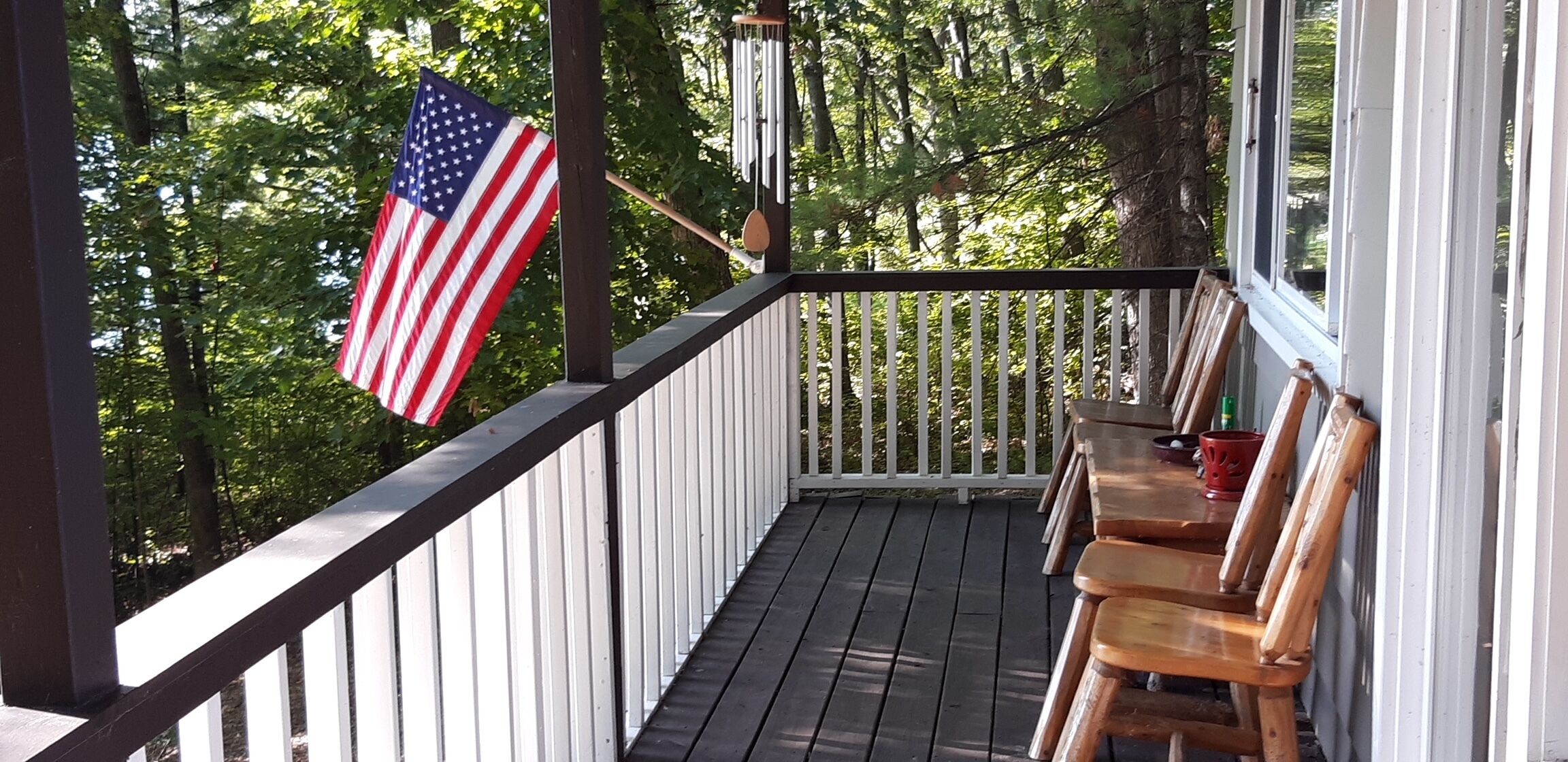 A wooden deck with a railing, a bench, and an American flag.