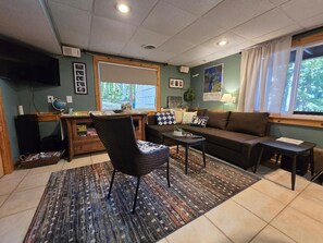 A furnished living room with a sofa, armchair, coffee table, and a television. - Lake house with game room perfect for enjoying every season (Fife Lake)