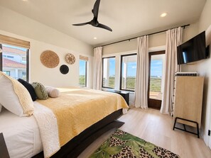 Een slaapkamer met een bed, een plafondventilator, een televisie en uitzicht op het omliggende landschap.