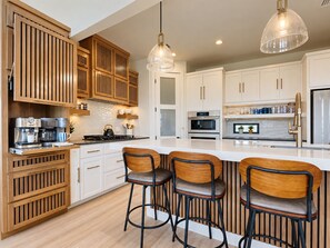 Een moderne keuken met houten kastjes, een centraal eiland met barstoelen, roestvrijstalen apparatuur en hangende verlichting.