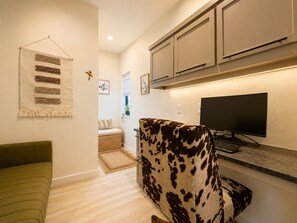 Ein modernes Wohnzimmer mit einem grünen Sofa, einem Schaukelstuhl aus Rindsleder, einem Flachbildfernseher und einer Küchenzeile mit Schränken und einer Arbeitsplatte.