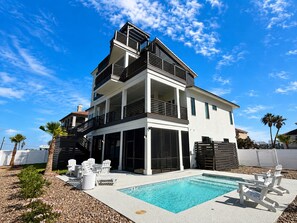 Una moderna casa a due piani con piscina, area relax esterna e cielo azzurro intenso.
